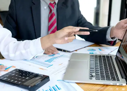 Two people with spreadsheets, calculators, and computers spread around them.